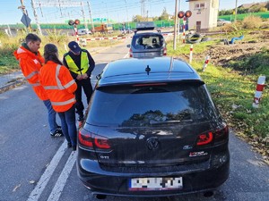 Zdjęcie przedstawia: 
Dwa samochody stojące przed zamkniętym przejazdem kolejowym, przy jednym z aut stoją przedstawiciele Kolei Śląskich wraz z funkcjonariuszem policji.