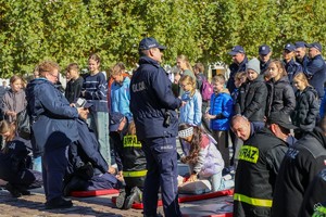 Na zdjęciu umundurowani policjanci wraz z dziećmi ćwiczącymi prowadzenie resuscytację na fantomie