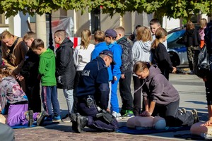 Na zdjęciu umundurowany policjant wraz z dziećmi ćwiczącymi prowadzenie resuscytację na fantomie