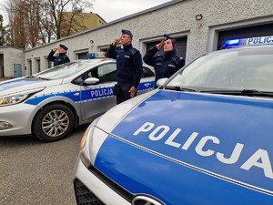 Zdjęcie przedstawia: salutujących policjantów przy radiowozach.