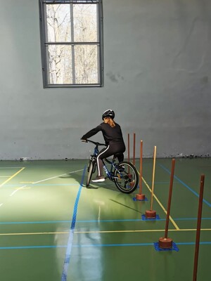 Zdjęcie przedstawia: dziewczynkę na rowerze wykonującą slalom między pachołkami