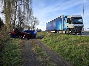 Zdjęcie przedstawia: dachujący pojazd osobowy pozbawiony drzwi oraz rozbity pojazd ciężarowy