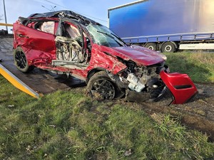 Zdjęcie przedstawia: zmiażdżony pojazd osobowy widziany z prawej strony na lawecie
