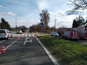 Zdjęcie przedstawia: trzy wozy straży pożarnej stojące na poboczu oraz strażaków w miejscu wypadku