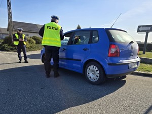 Zdjęcie przedstawia: funkcjonariusza policji rozmawiającego z kierowcą niebieskiego pojazdu osobowego