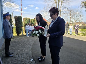 Zdjęcie przedstawia: Dwie kobiety trzymające wieniec i znicz.