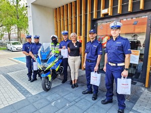 Zdjęcie przedstawia grupę umundurowanych policjantów, kobietę i motocykl służbowy.