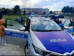 Zdjęcie przedstawia: radiowóz policyjny z otwartymi, przednimi drzwiami.