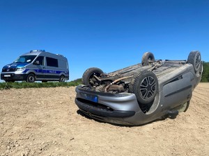 Zdjęcie przedstawia: auto po dachowaniu i radiowóz policji.