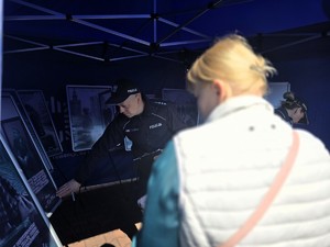Zdjęcie przedstawia: policjanta, który wskazuje na plakat.