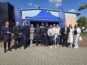 Zdjęcie przedstawia: grupę ludzi przed namiotem policji.