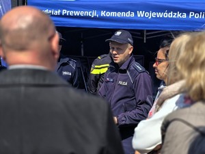 Zdjęcie przedstawia: osobę umundurowana rozmawiającą z ludźmi.