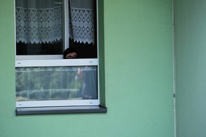 Zdjęcie przedstawia: mężczyznę wyglądającego przez okno