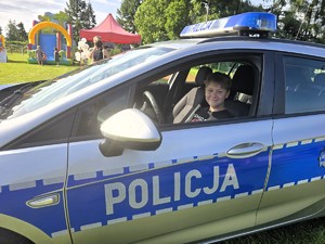 Zdjęcie przedstawia: dziecko siedzące w policyjnym radiowozie