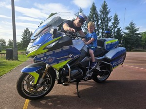 Zdjęcie przedstawia: policjanta, który pokazuje dziecku policyjny motocykl