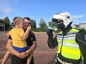 Zdjęcie przedstawia: policjanta w kasku i dziecko z rodzicem