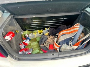 Zdjęcie przedstawia: otwarty bagażnik a w nim ubrania i puszki po piwie.