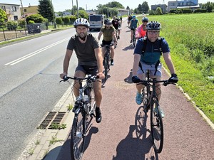 Zdjęcie przedstawia: grupę ludzi jadącą w kolumnie na rowerach.