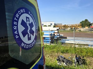 Zdjęcie przedstawia: karetkę pogotowia i motocykl leżący w rowie przy drodze.