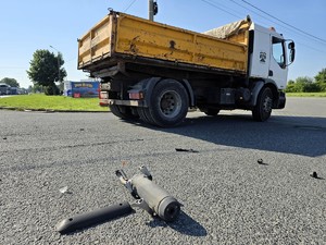 Zdjęcie przedstawia: odłamki motocyklu leżące na drodze, obok stoi ciężarówka.