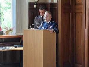 Zdjęcie przedstawia: umundurowanego policjanta przemawiającego z mównicy.