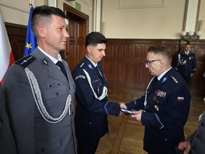 Zdjęcie przedstawia: policjanta ściskającego dłoń innego policjanta.