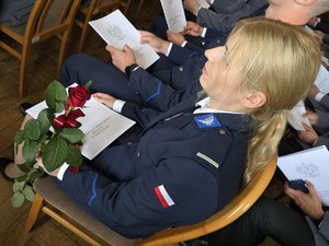 Zdjęcie przedstawia: policjantkę trzymająca teczkę i różę.
