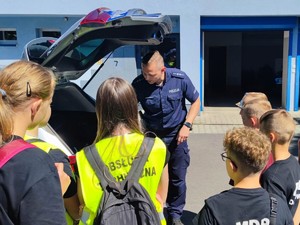 Zdjęcie przedstawia: policjanta pokazującego dzieciom radiowóz.
