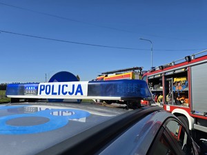 Zdjęcie przedstawia: dach policyjnego radiowozu i wozy strażackie.