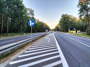 Zdjęcie przedstawia: drogę dwupasmową i znak nakazu jazdy prosto lub w prawo.