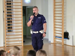 Zdjęcie przedstawia: osobę umundurowaną trzymającą mikrofon w ręce.