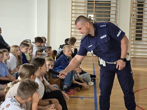 Zdjęcie przedstawia: osobę umundurowana, która trzyma mikrofon przed odpowiadająca dziewczynką.