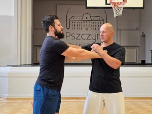 Zdjęcie przedstawia: prowadzącego, który trzyma uczestnika za rękę i szyję.