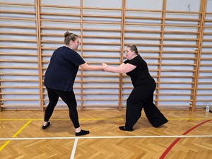 Zdjęcie przedstawia: kobietę trzymająca jedną z uczestniczek za nadgarstki.