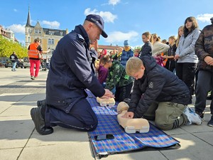 zdjęcie przedstawia: umundurowanego policjanta pokazującego jak złożyć ręce do reanimacji.