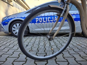 Zdjęcie przedstawia: koło roweru, z tyłu radiowóz.