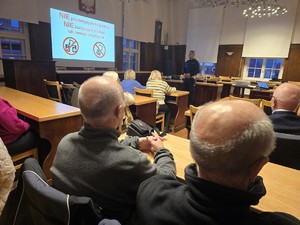 Zdjęcie przedstawia: uczestników spotkania i umundurowanego policjanta podczas pogadanki.