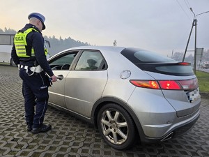 Zdjęcie przedstawia umundurowanego policjanta oraz samochód osobowy.