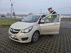 Zdjęcie przedstawia umundurowanego policjanta oraz samochód osobowy.