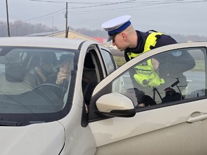 Zdjęcie przedstawia umundurowanego policjanta oraz samochód osobowy.