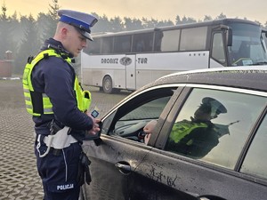 Zdjęcie przedstawia umundurowanego policjanta oraz samochód osobowy.