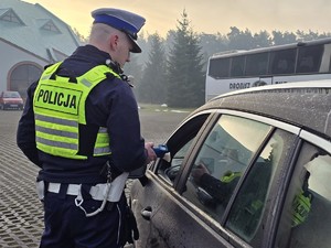 Zdjęcie przedstawia umundurowanego policjanta oraz samochód osobowy.