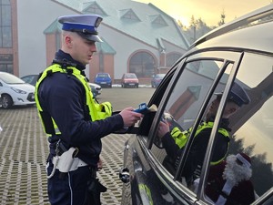 Zdjęcie przedstawia umundurowanego policjanta oraz samochód osobowy.