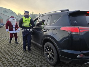 Zdjęcie przedstawia umundurowanego policjanta, uczestnika akcji oraz samochód osobowy.