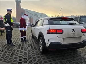 Zdjęcie przedstawia umundurowanego policjanta, uczestników akcji oraz samochód osobowy.
