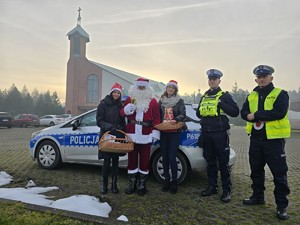 Zdjęcie przedstawia dwóch policjantów, uczestników akcji oraz radiowóz.