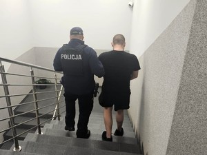 Zdjęcie przedstawia umundurowanego policjanta z osobą zatrzymaną.