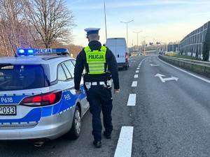 Zdjęcie przedstawia umundurowanego policjanta oraz oznakowany radiowóz.