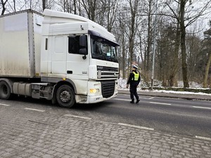 Zdjęcie przedstawia umundurowanego policjanta oraz samochód ciężarowy.