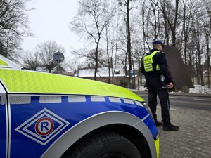 Zdjęcie przedstawia umundurowanego policjanta oraz oznakowany radiowóz.